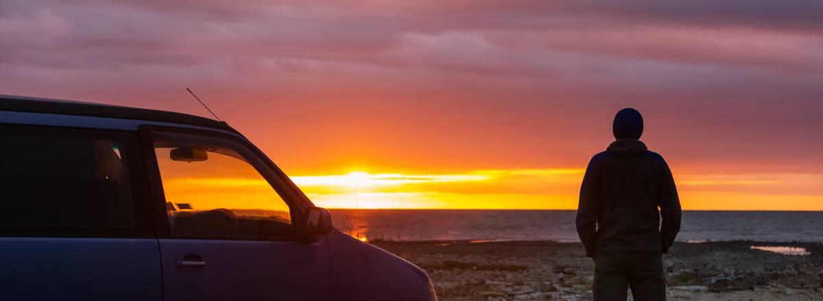 mand ved siden af bil kigger på solnedgang